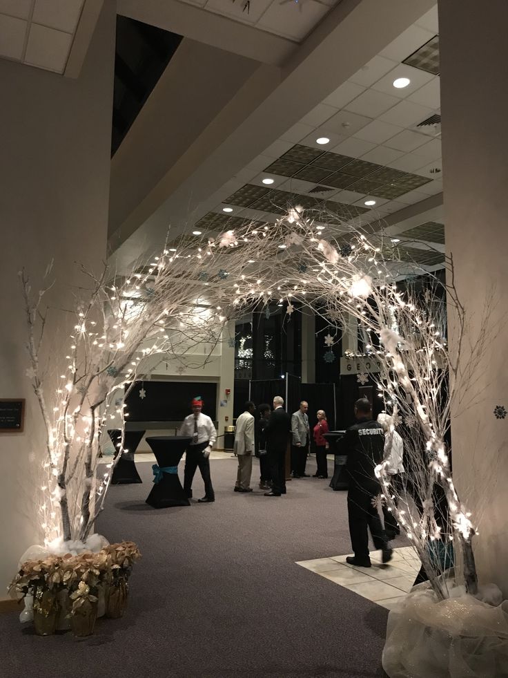 people are walking through an open area with lights on the ceiling and trees in the center