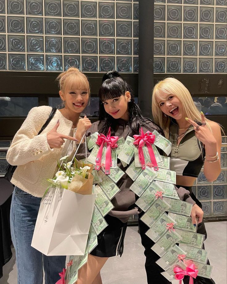 three women standing next to each other holding shopping bags with money in them and pointing at the camera