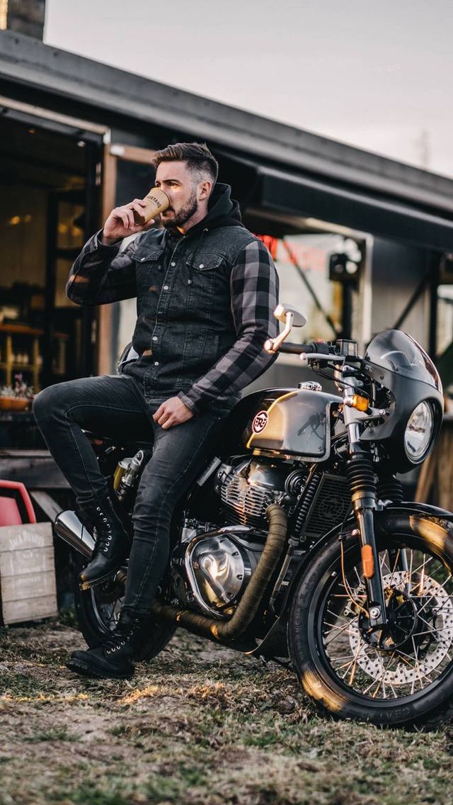 a man is sitting on his motorcycle and eating something out of his mouth as he looks off to the side