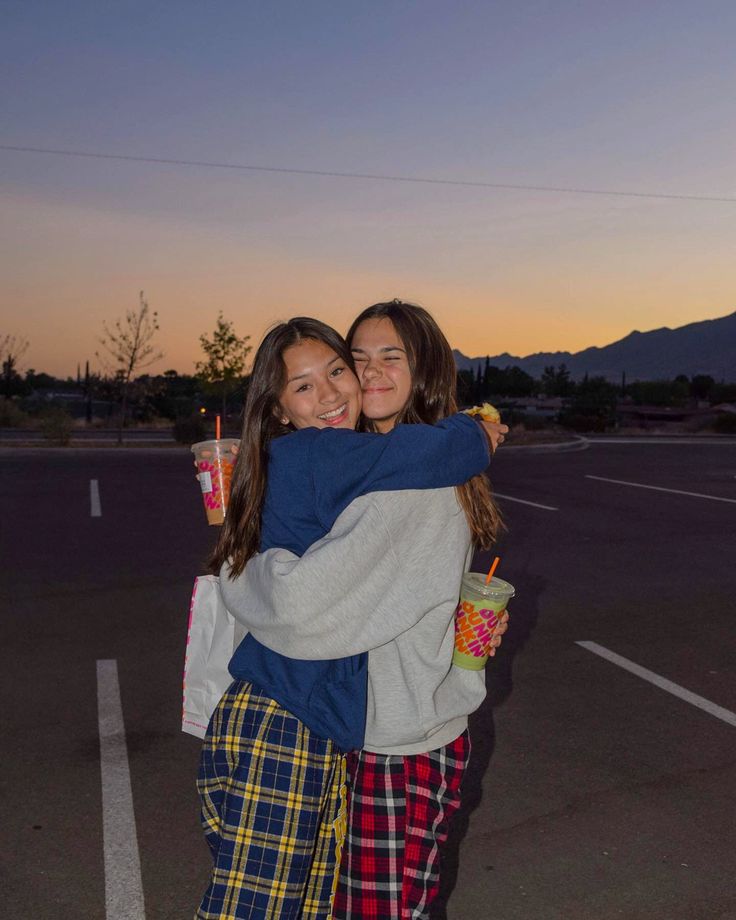 two girls hugging each other in the middle of a parking lot at sunset with mountains in the background