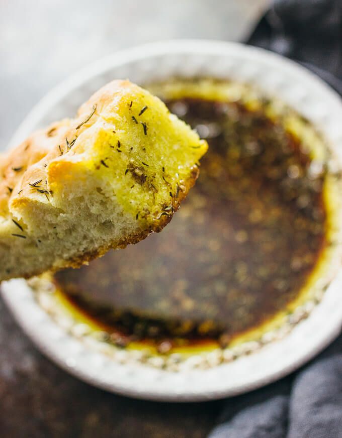 a piece of bread is being held up over a bowl of dipping sauce with a spoon