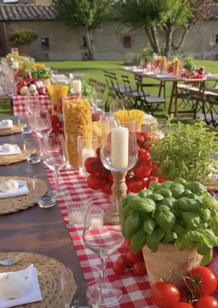 a long table is set with red and white checkered cloths, wine glasses, candles, tomatoes, cornbreads, and other food