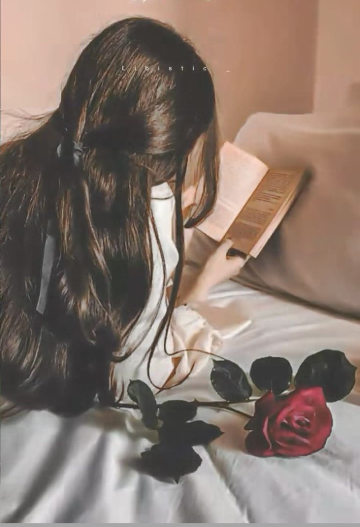 a woman laying on top of a bed next to a red rose in her hair