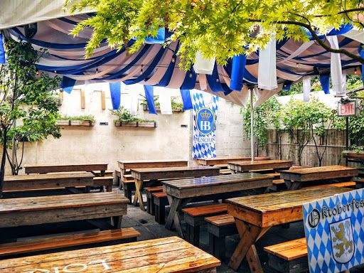 an outdoor restaurant with wooden tables and benches under a blue tarp covered awning