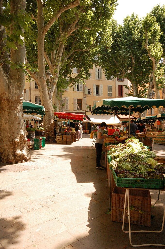 an outdoor market with lots of fruit and veggies for sale in the shade