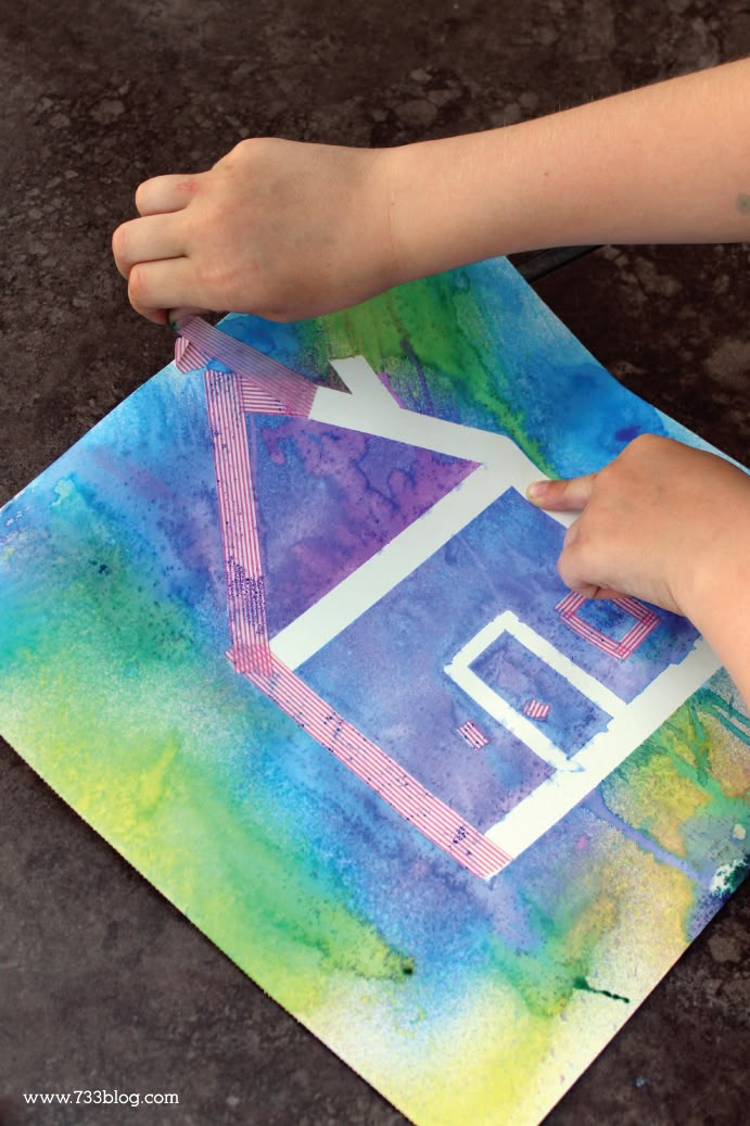 a child's hand is painting a house on a piece of paper