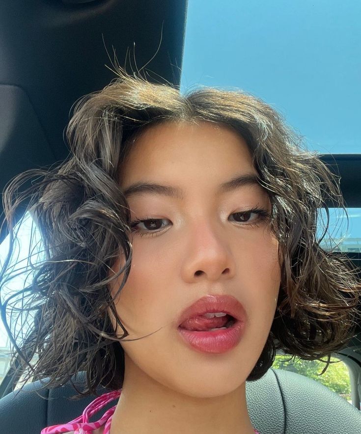 a woman with curly hair sitting in the back seat of a car and making a funny face