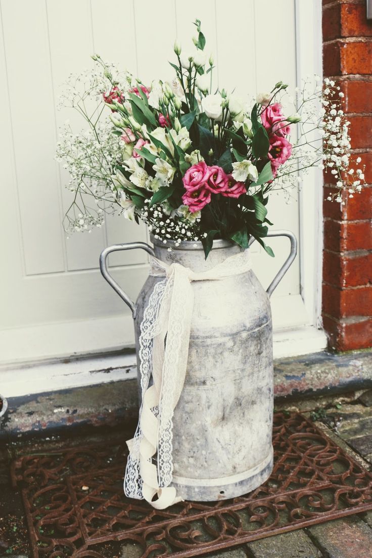 a metal watering can with pink and white flowers in it sitting on a door mat