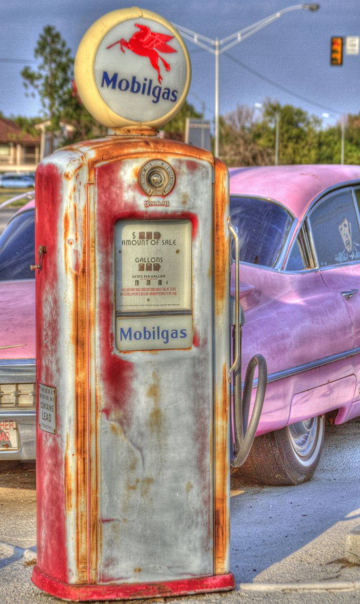 an old gas pump sitting next to a pink car