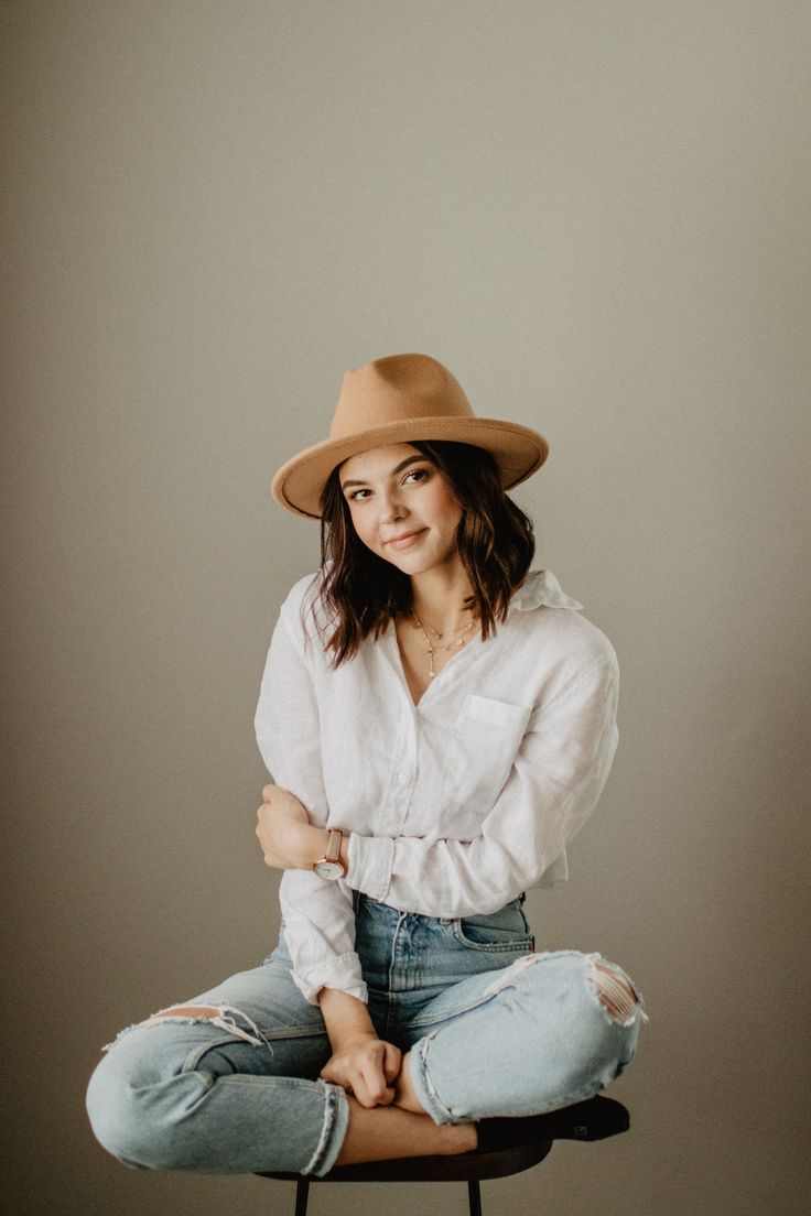 a woman sitting on top of a chair with her arms crossed and wearing a hat