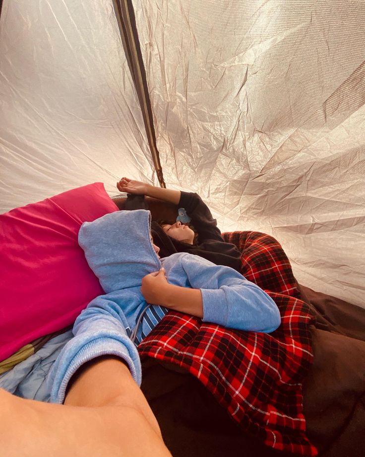 a person laying on top of a bed next to a white tent covered in tarp