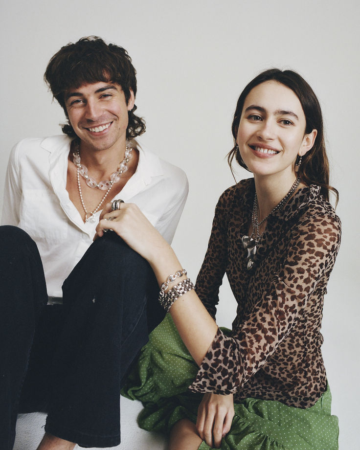 a man and woman sitting next to each other on a white surface smiling at the camera