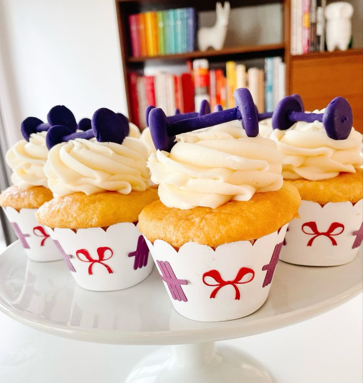 three cupcakes with white frosting and purple bows on them sitting on a cake plate