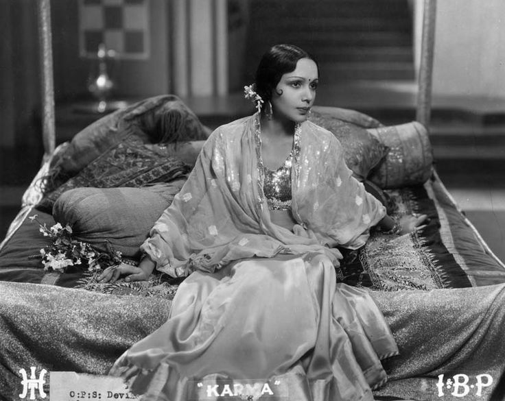 a woman sitting on top of a bed wearing a dress and jewelry in an old photo