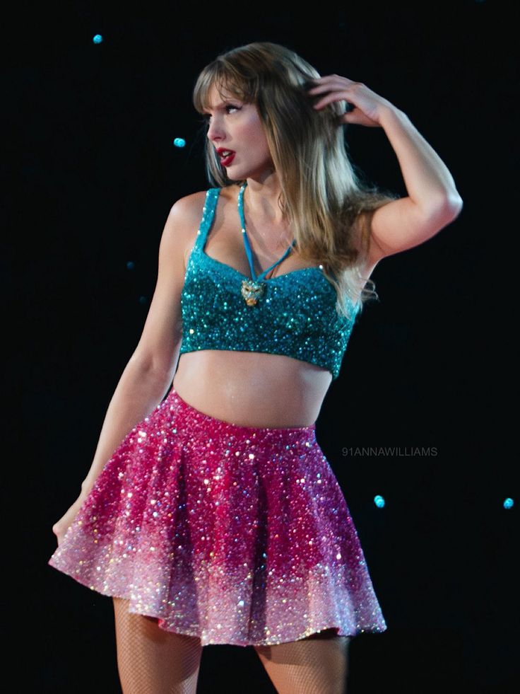 a woman in a short skirt and crop top on stage with her hands behind her head