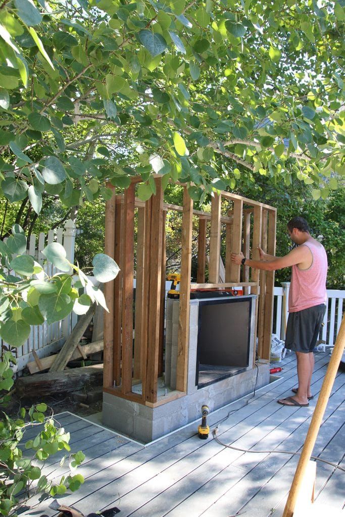 a man standing on top of a wooden deck next to a tv set in the woods