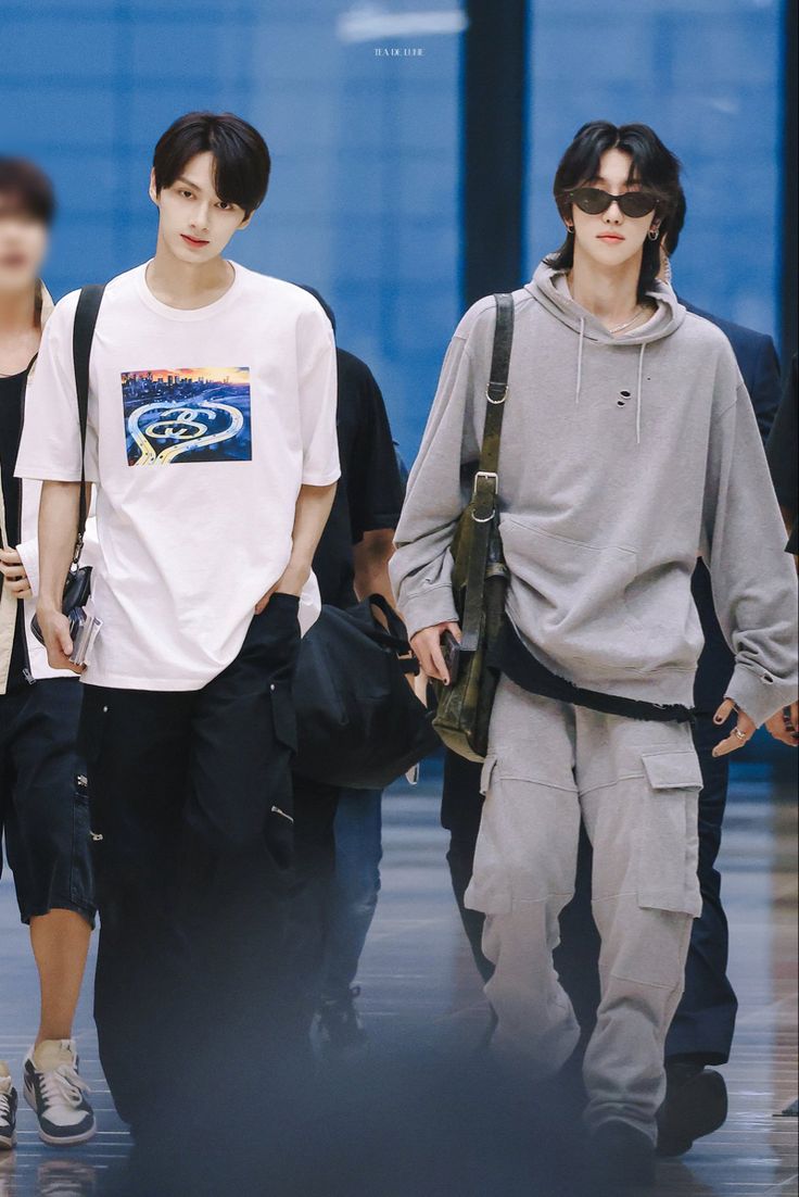 two young men walking down the street with one carrying a black bag and another wearing a white t - shirt