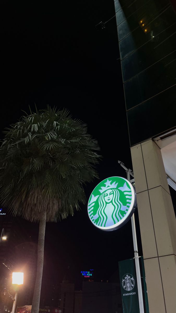 a starbucks sign on the side of a building next to a palm tree at night