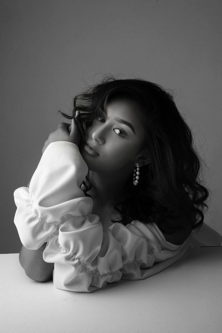 a woman sitting on top of a table next to a white wall with her hand under her chin