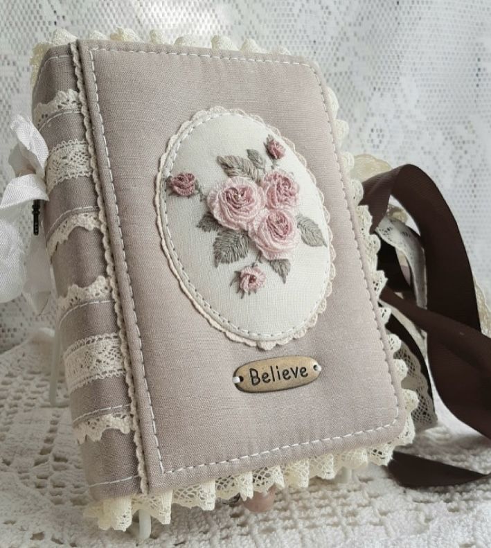 a small book with flowers on it sitting on a lace doily