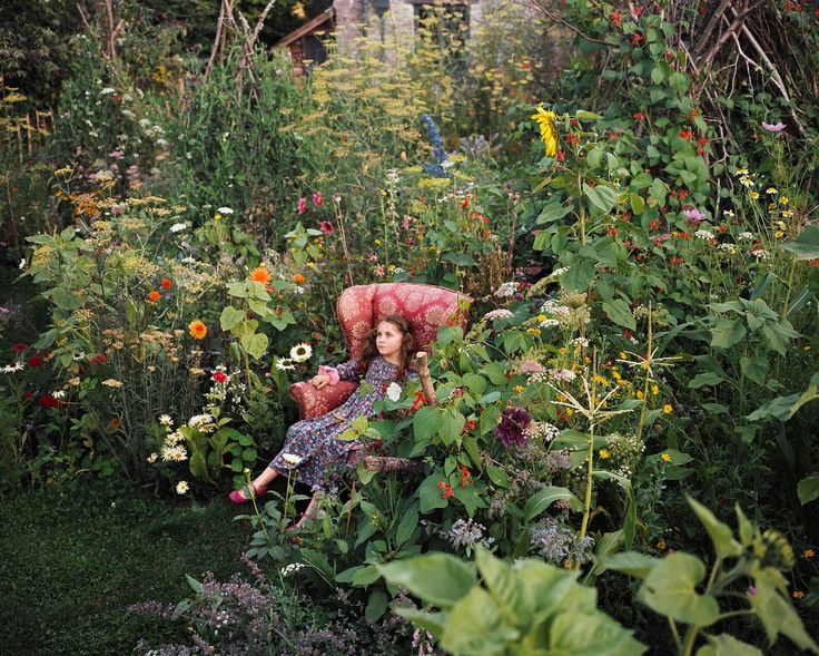 a woman sitting on a chair in the middle of a garden filled with lots of flowers