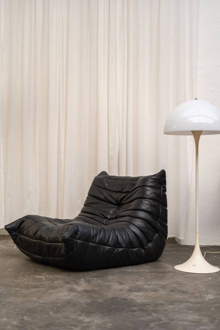 a black bean bag chair sitting next to a white lamp on a gray concrete floor