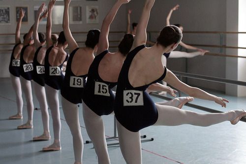 a row of women in leotards are doing ballet moves with numbers on their backs