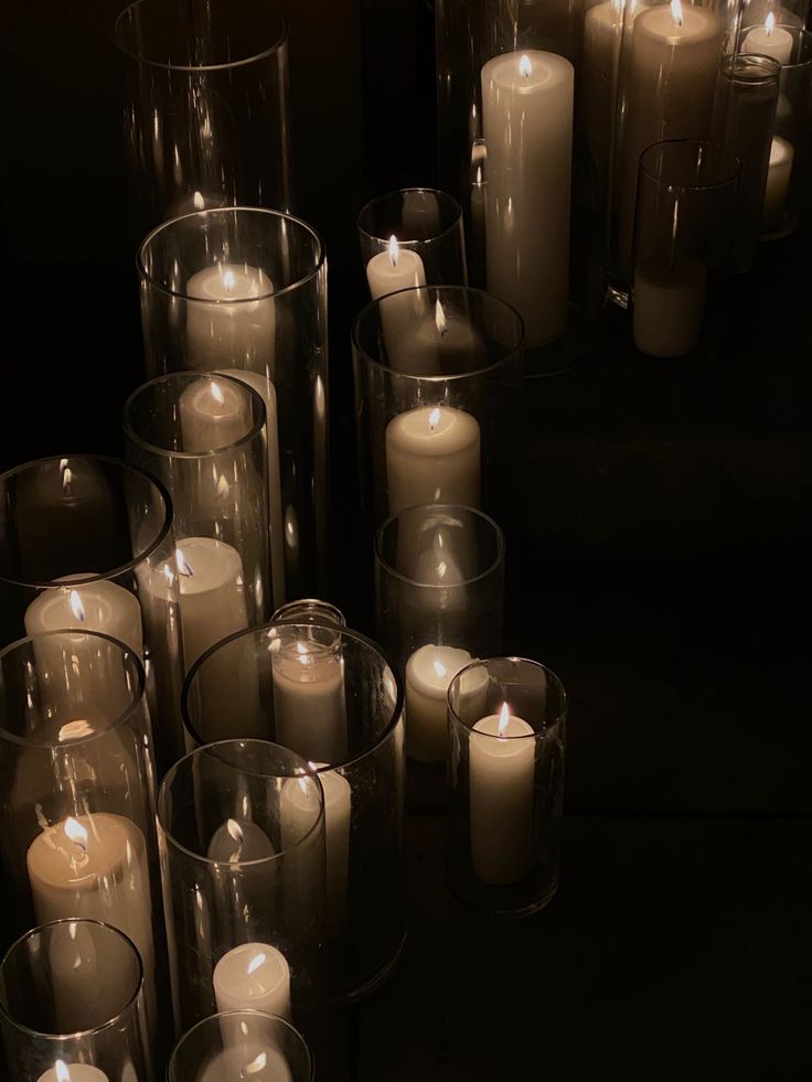 many lit candles are arranged in rows on the floor next to each other, with dark background