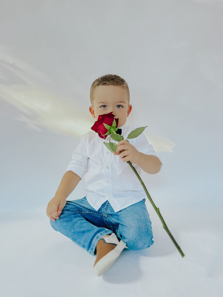 a young boy sitting on the ground holding a rose