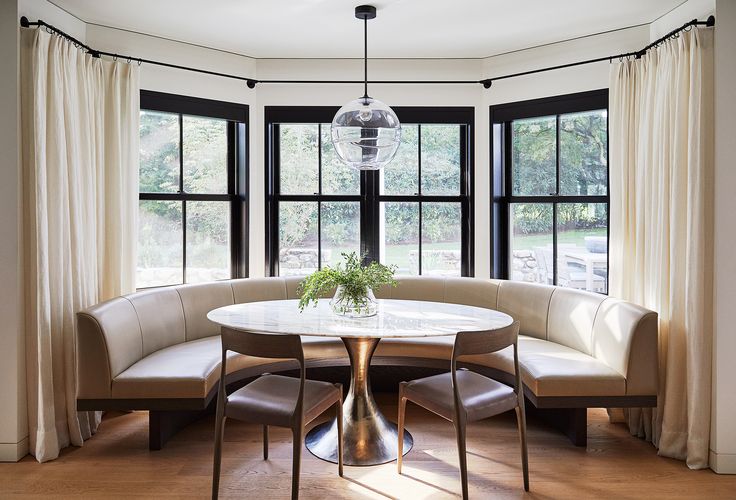 a round table with four chairs and a bench in front of two large windows next to each other