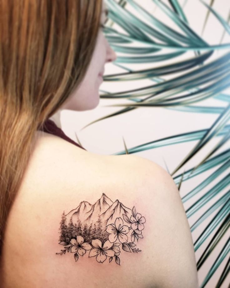 a woman's shoulder with flowers and mountains in the background on her left arm