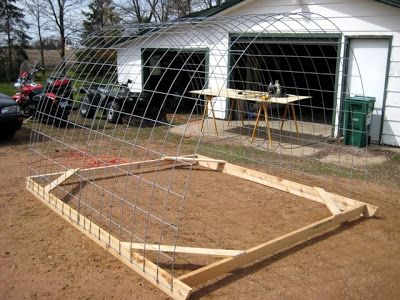 a large wooden frame sitting in the middle of a dirt field next to a garage