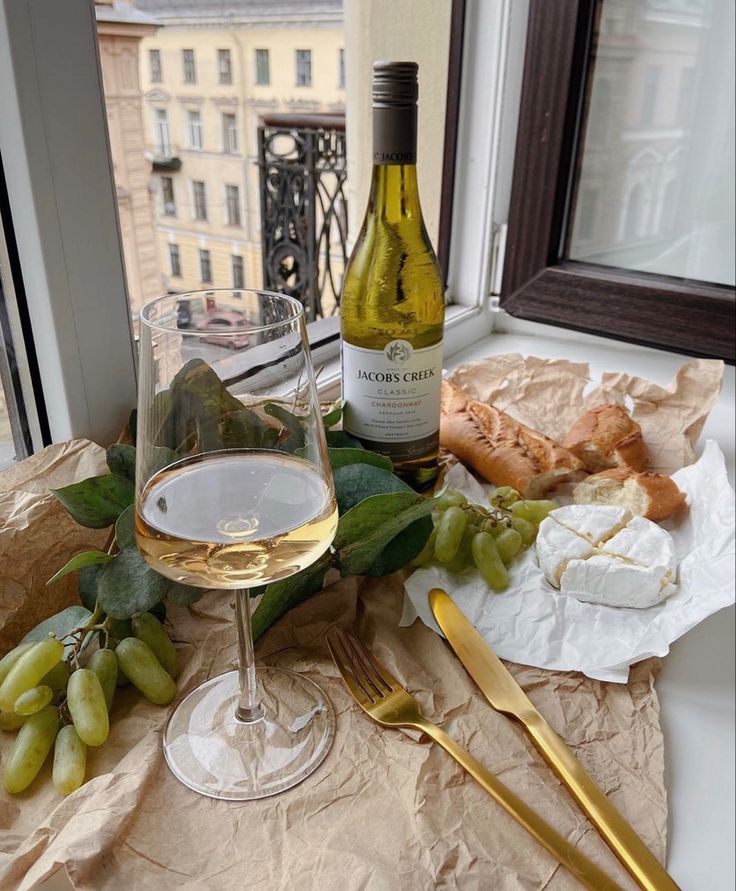 a glass of wine, cheese and grapes on a table with a window in the background