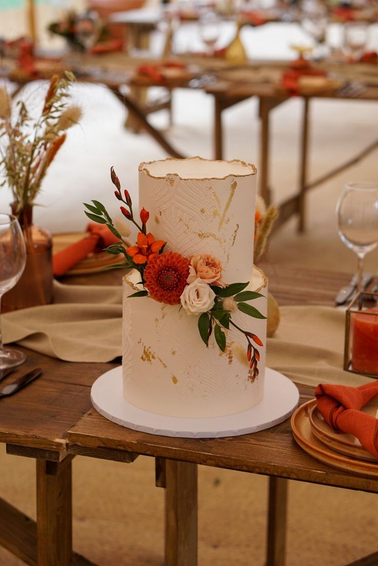 a white wedding cake with orange flowers on the top is sitting on a wooden table