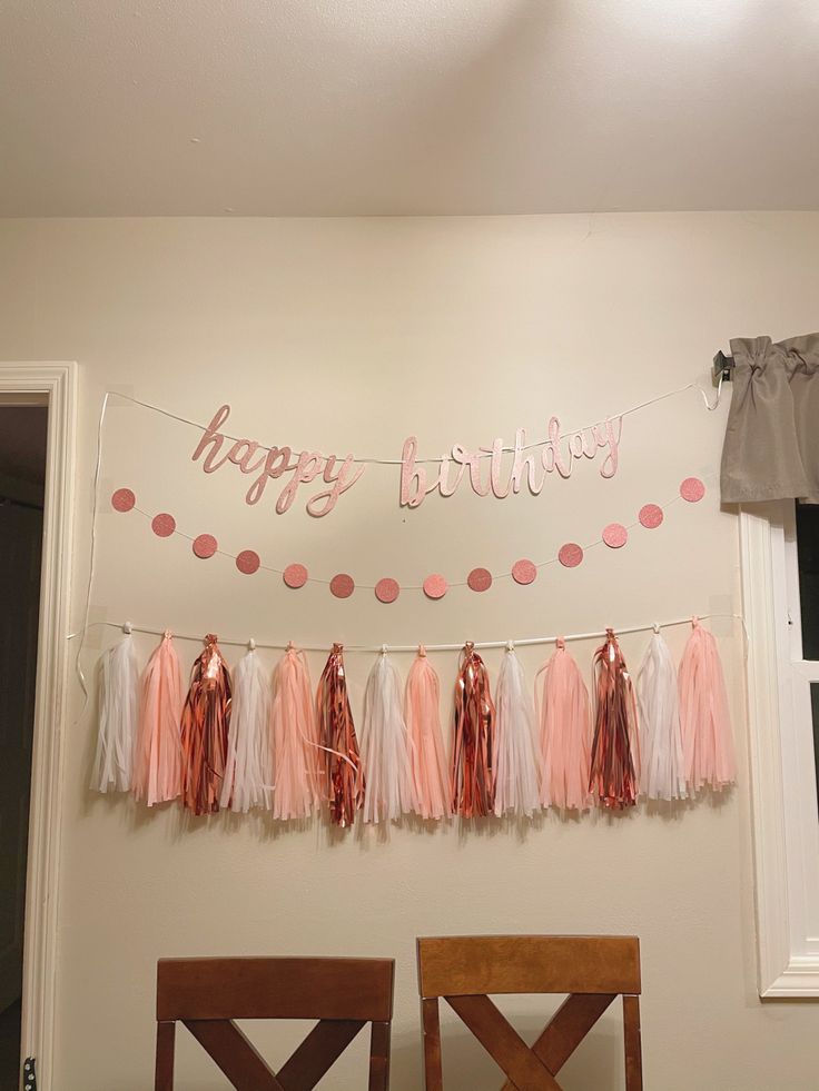 a happy birthday banner with pink and white tissue pom poms hanging from the ceiling