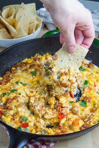 a person dipping a tortilla chip into a skillet filled with mexican food