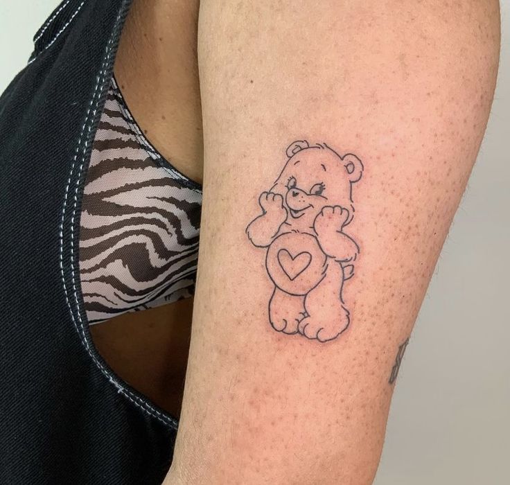 a woman's arm with a small tattoo of a teddy bear holding a heart