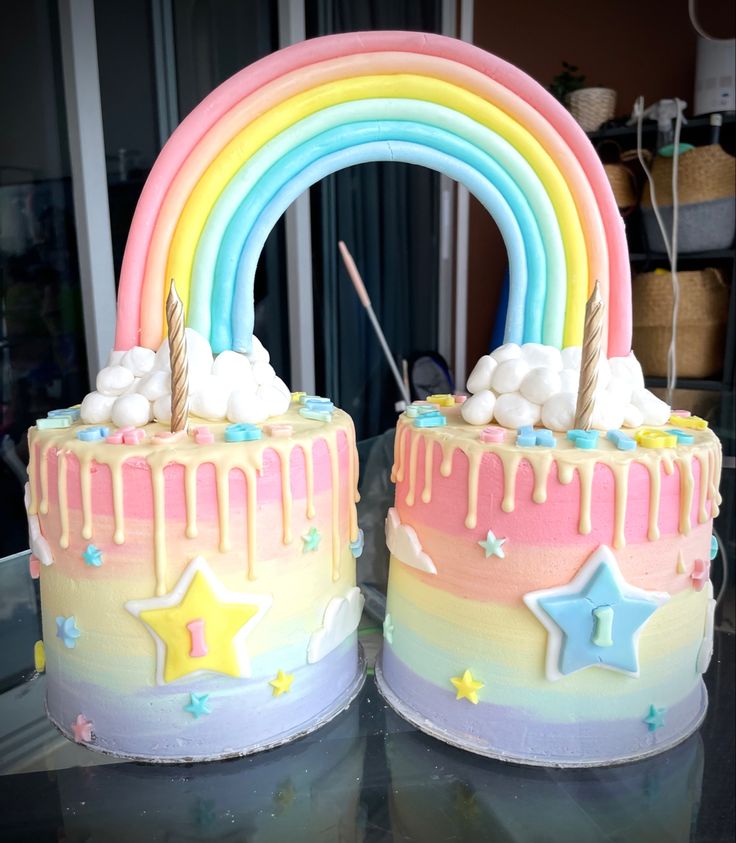 two cakes decorated with rainbow icing and sprinkles are on a table