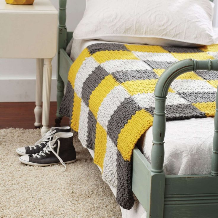 a bed with a yellow blanket and black sneakers on the floor next to an end table