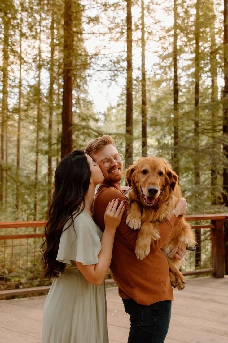 a man and woman are holding a dog in their arms as they stand on a wooden deck