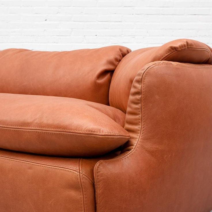 a brown leather couch sitting in front of a white brick wall