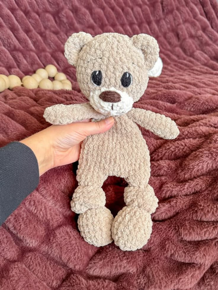 a person is holding a small teddy bear on a bed with purple sheets and beads