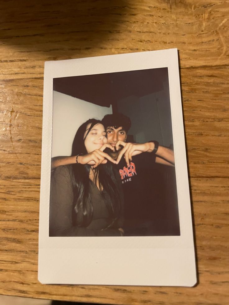 two people making a heart shape with their hands on a wooden table next to each other