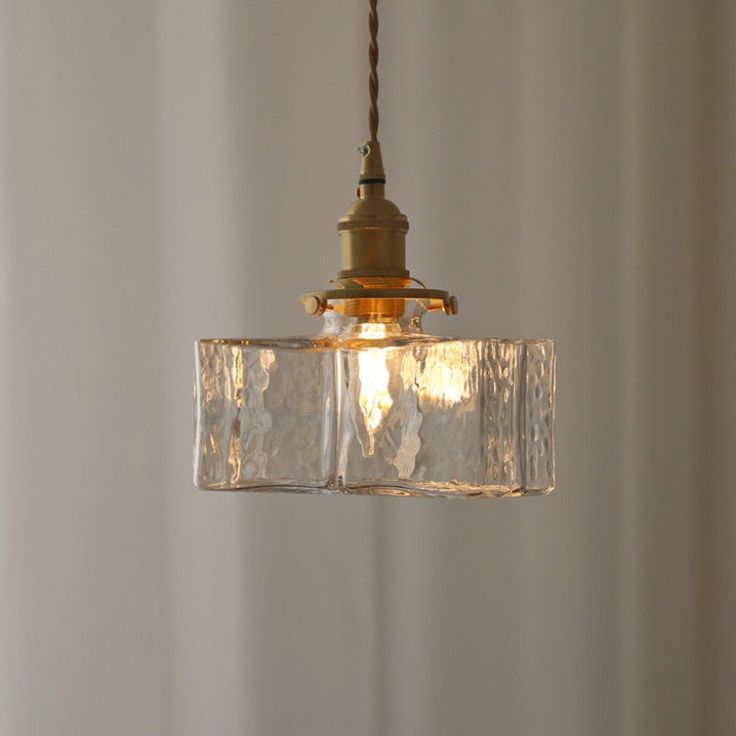 a clear glass light fixture hanging from a metal ceiling hook in a white walled room