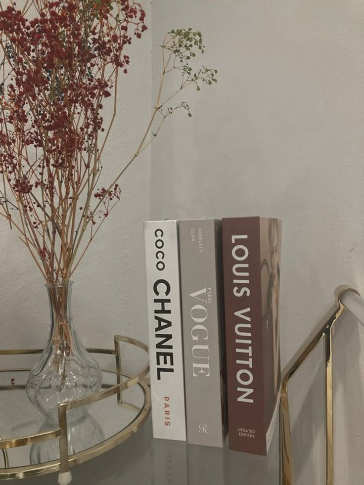 two books are sitting on a glass table next to a vase with flowers in it