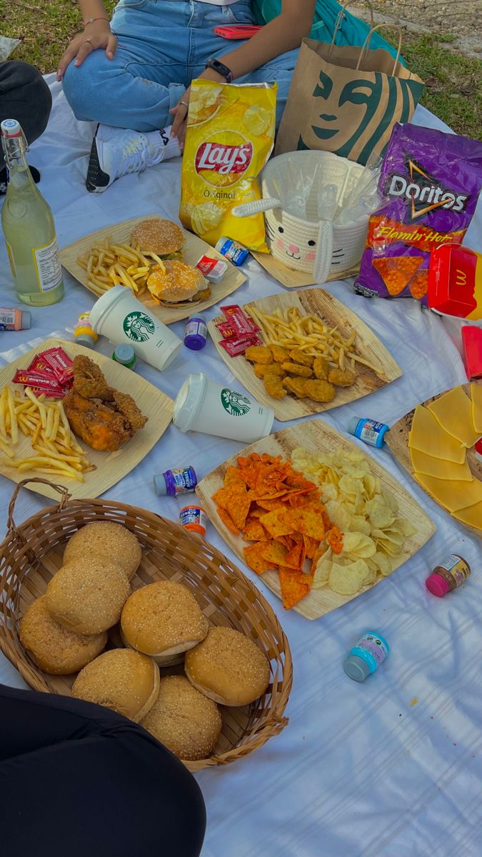 people sitting at a table with food and drinks on it, including breads, chips, and soda