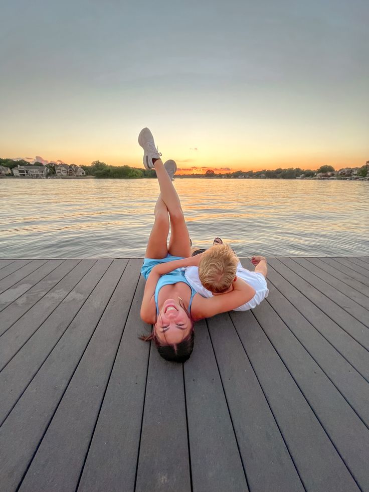 a woman laying on top of a wooden pier next to a body of water at sunset