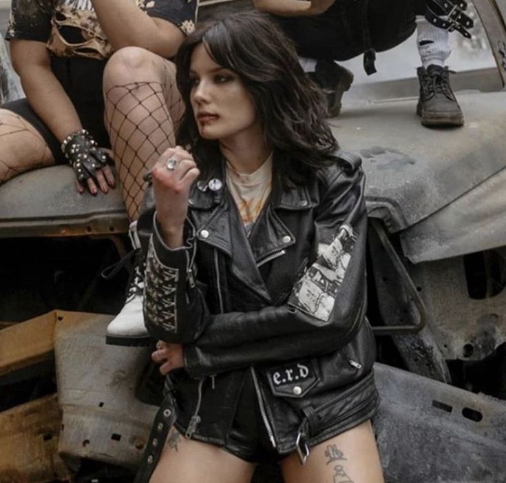 a woman sitting on top of a car next to other women in short shorts and boots