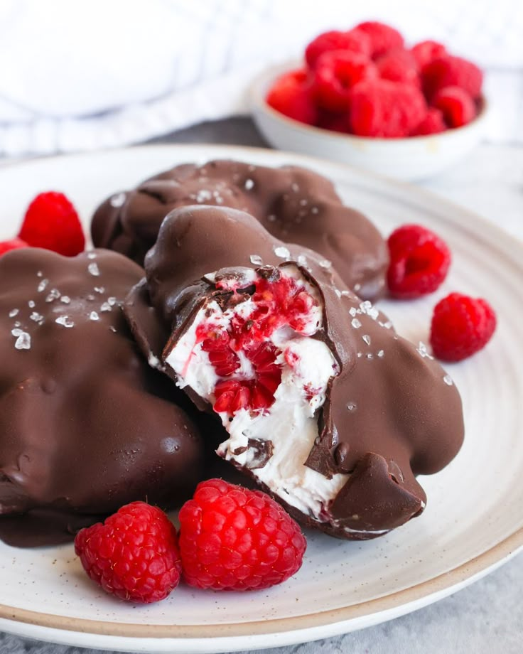 chocolate covered desserts with raspberries on a plate next to some strawberries