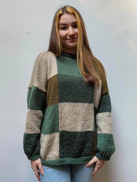 a woman standing in front of a white wall wearing a green and beige checkered sweater